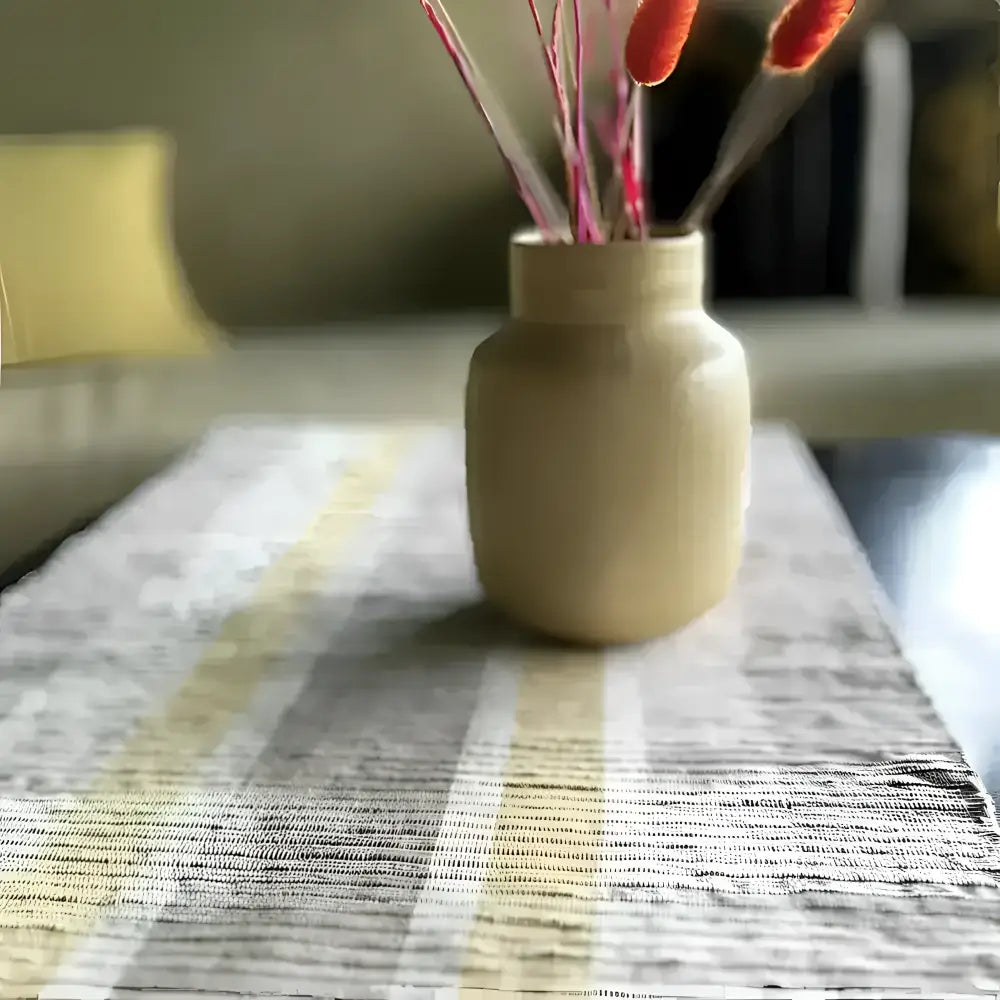 Beige ceramic vase with pink and orange dried flowers on handwoven vetiver table runner gray and beige stripes