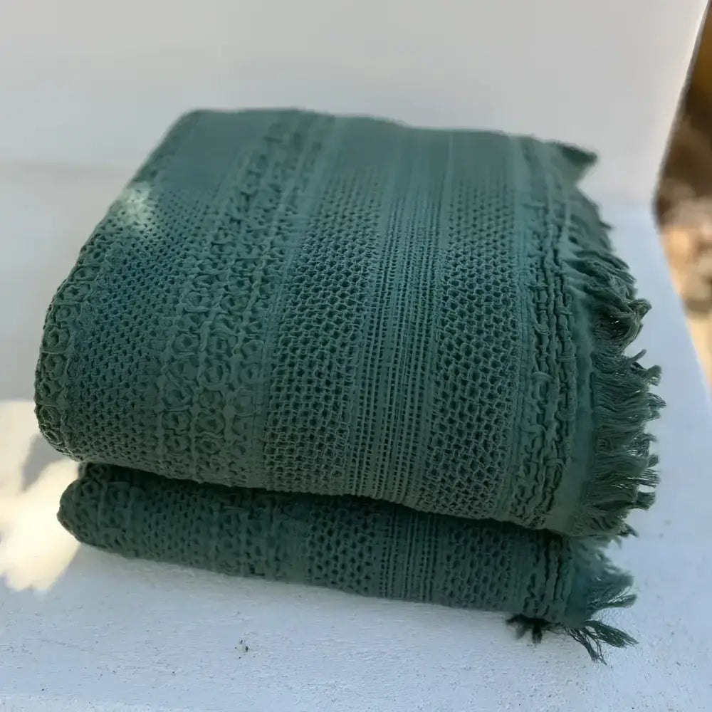 Folded green textured blanket on a white surface with a blurred background
