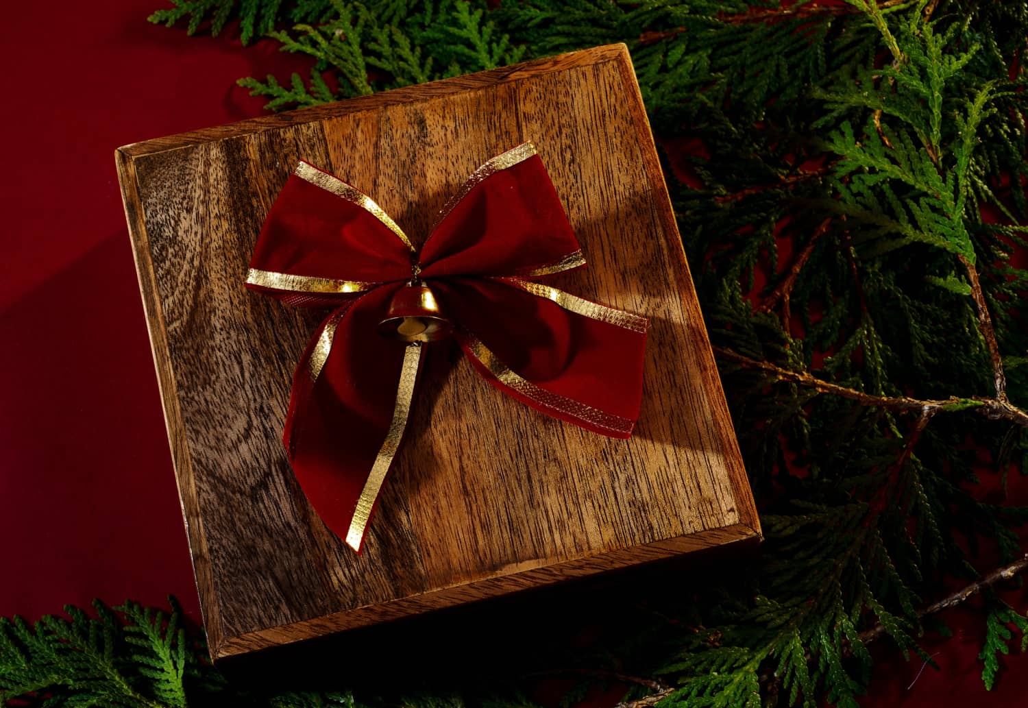 wooden box with a red bow and bell, surrounded by evergreen branches