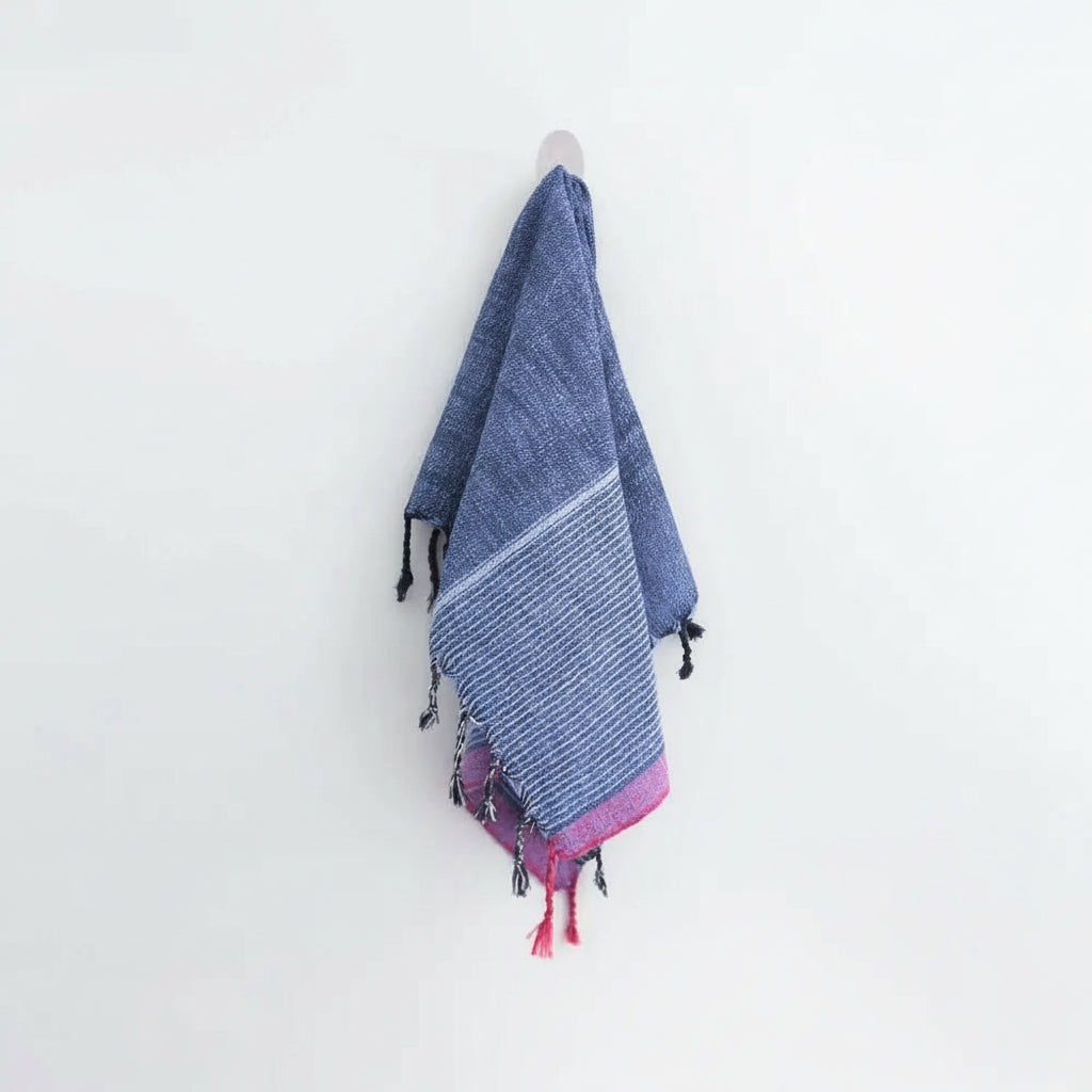 Indigo Tribeca handmade hand towel with blue and red stripes, pink tassels, and black pom-poms hanging on a hook