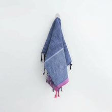 Indigo Tribeca handmade hand towel with blue and red stripes, pink tassels, and black pom-poms hanging on a hook