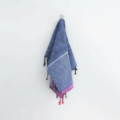 Indigo Tribeca handmade hand towel with blue and red stripes, pink tassels, and black pom-poms hanging on a hook