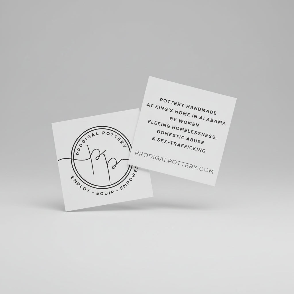 Two white business cards with black text on a stone surface