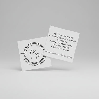 Two white business cards with black text on a stone surface