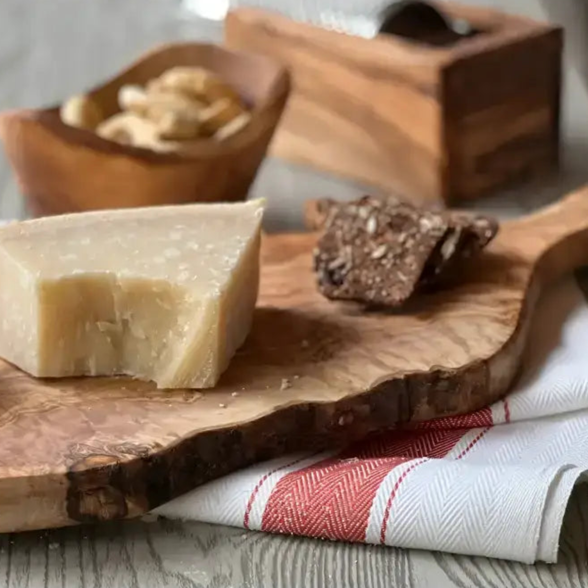 A wedge of pale yellow cheese on an italian olivewood cutting board with live bark edge and paddle handle