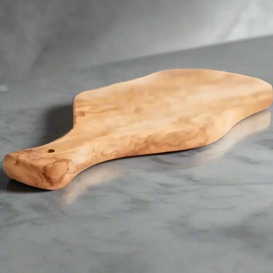 Light brown Italian Olivewood cutting board with bark edge and paddle handle for kitchen prep