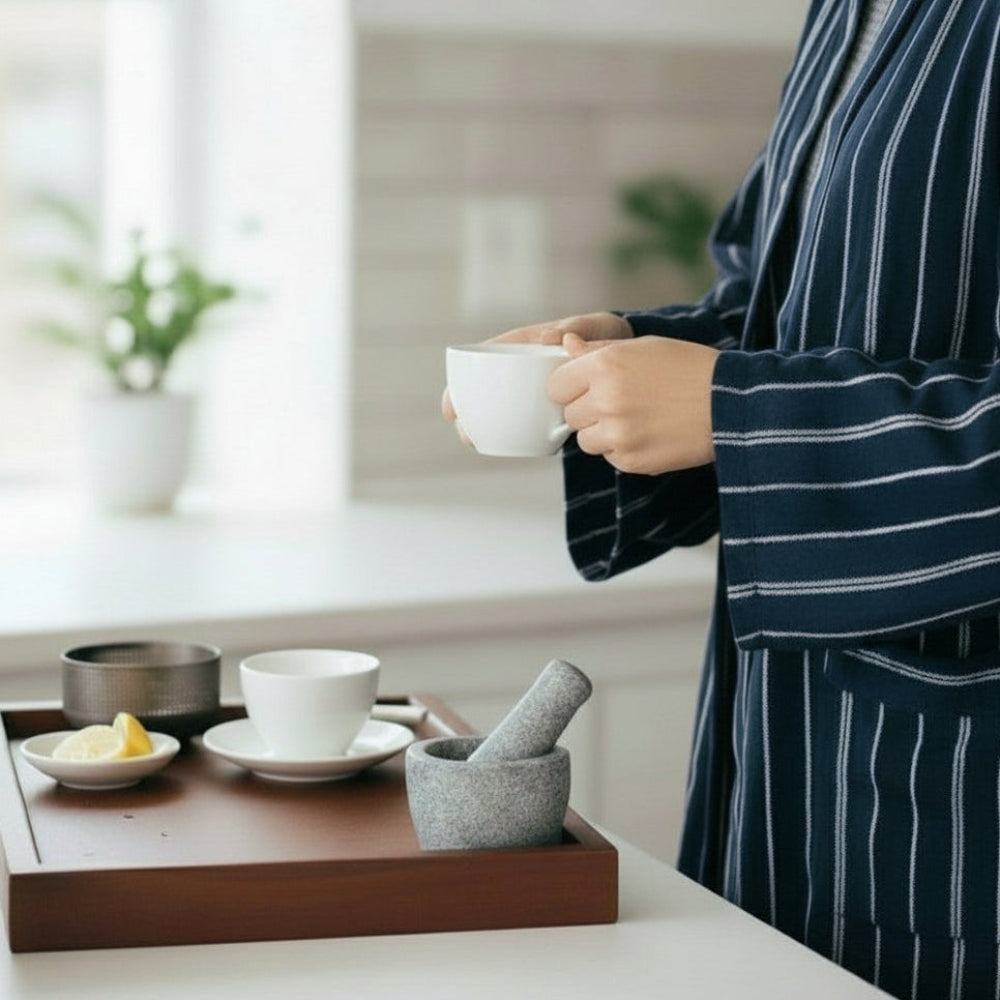 Person pouring tea from a teapot into a cup on a wooden tray with various tea accessories.