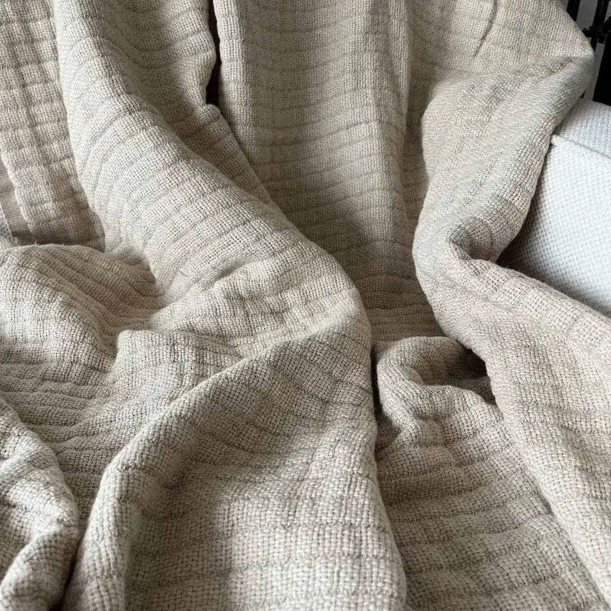 A beige colored linen throw on a white sofa.