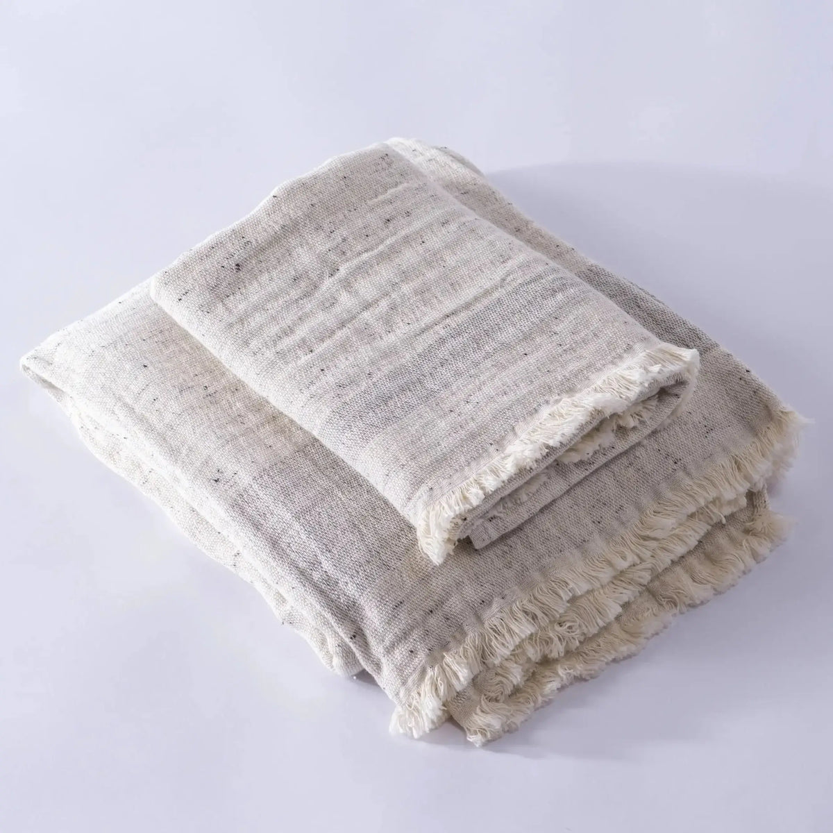 Two folded light-colored fringed muslin bath towels made from cotton nope yarn