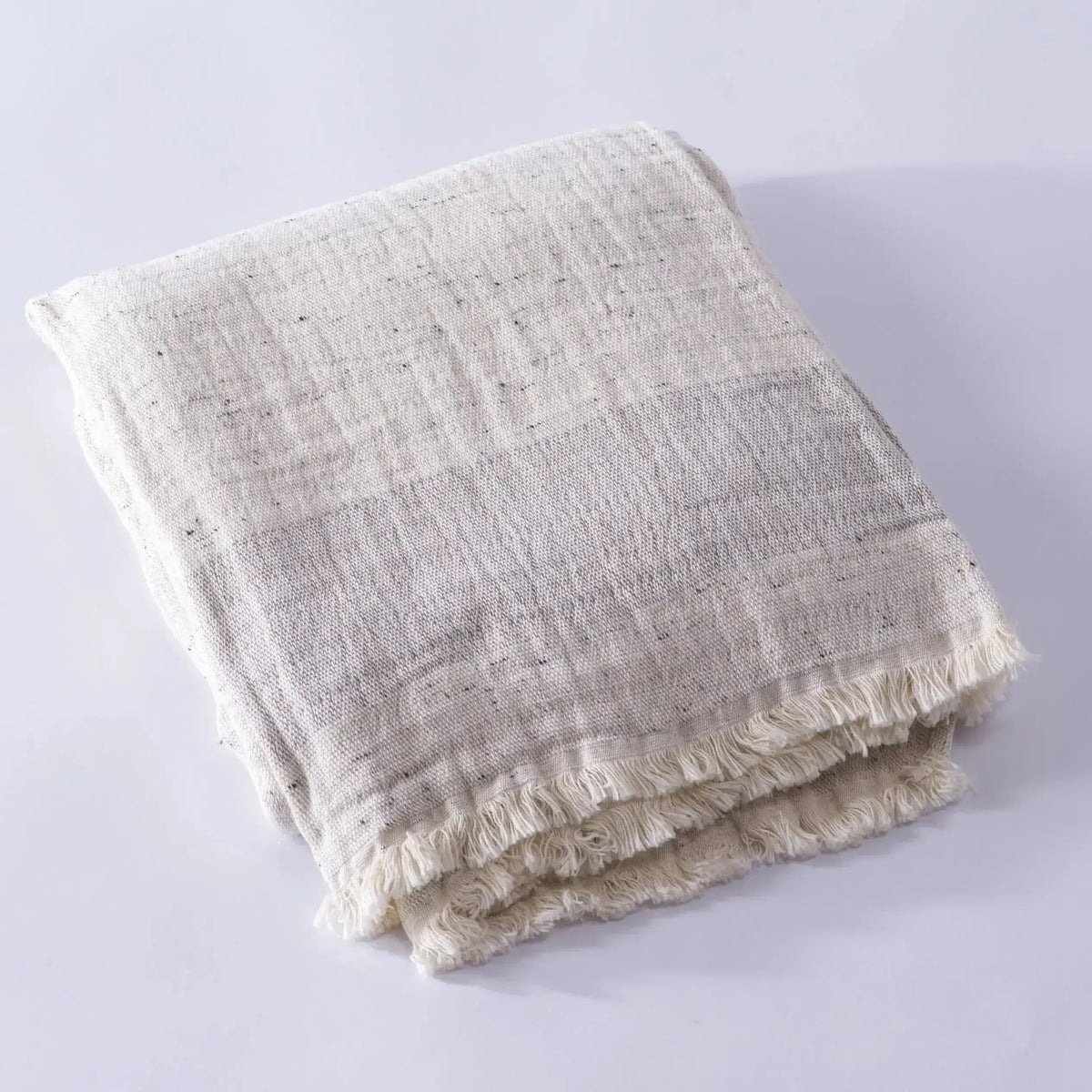 Folded light-colored muslin bath towel made from cotton nope yarn with fringed edges