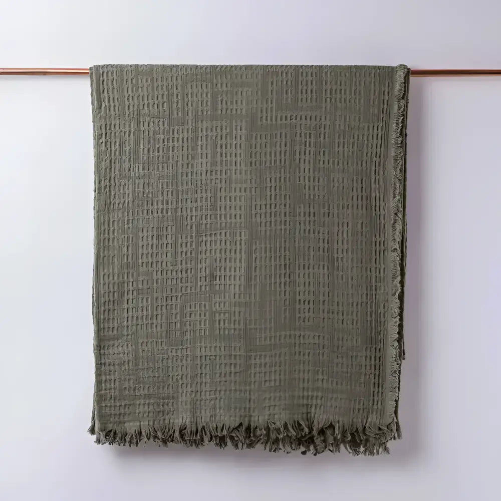 Olive green colored blanket hanging on light background