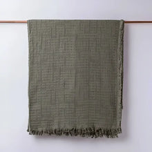 Olive green colored blanket hanging on light background