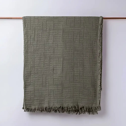 Olive green colored blanket hanging on light background
