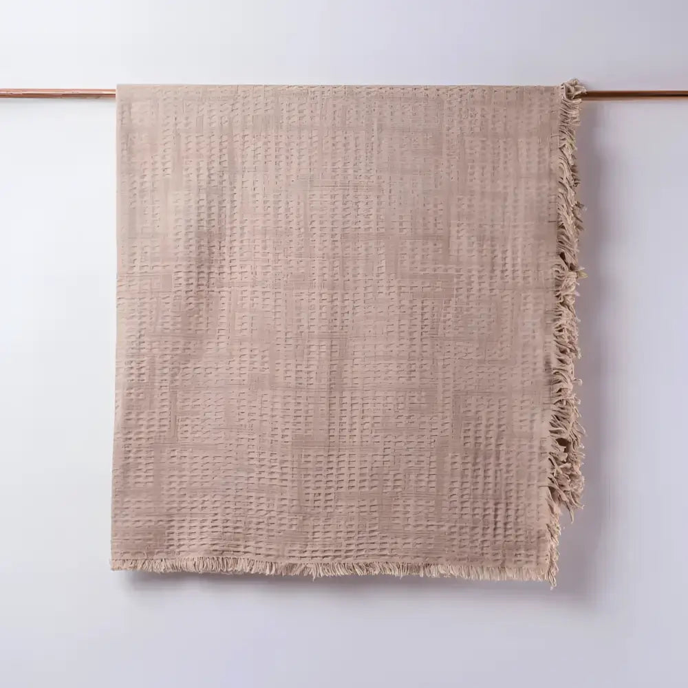 Taupe colored blanket hanging on light background