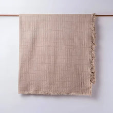 Taupe colored blanket hanging on light background