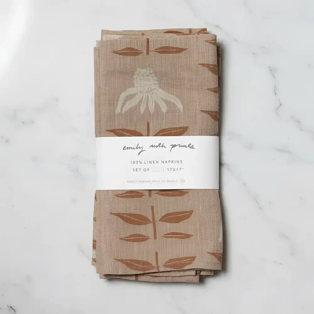 A set of two beige linen napkins with rust-colored leaves and off-white flower featuring hand-carved stamp designs