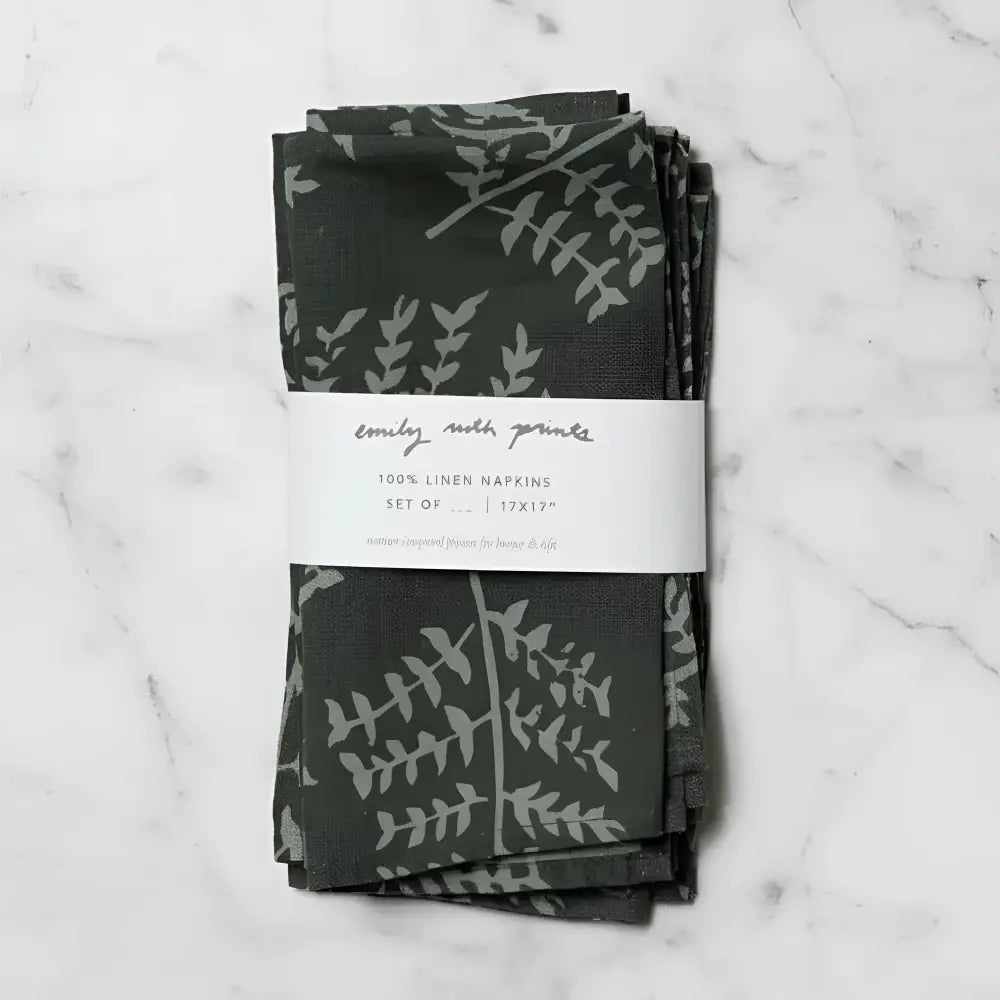 Two dark green linen napkins with subtle gray fern hand carved stamp designs neatly folded and bundled