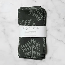 Two dark green linen napkins with subtle gray fern hand carved stamp designs neatly folded and bundled