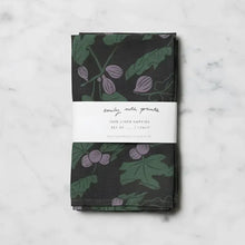 Two linen napkins in dark green with purple fig designs and leaves, wrapped in a white label band