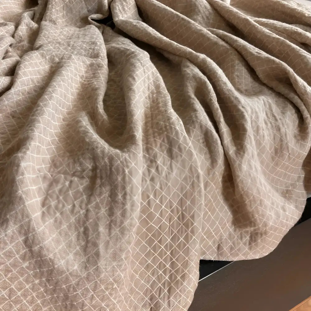 Linen throw blanket with an elegant diamond quilted design in beige and off-white tones.