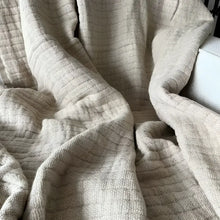 A beige colored linen throw on a white sofa.