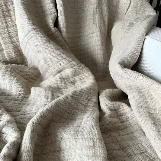 A beige colored linen throw on a white sofa.