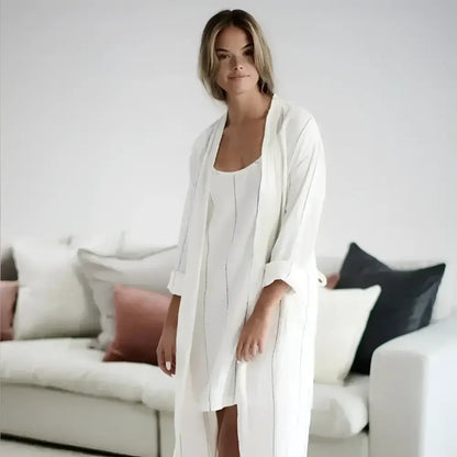 Woman wearing a white robe standing in a living room with a neutral color palette.
