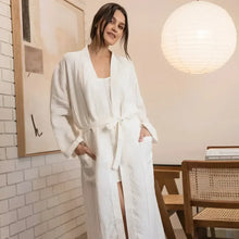 Woman wearing a white robe in a room with a lamp and chair.