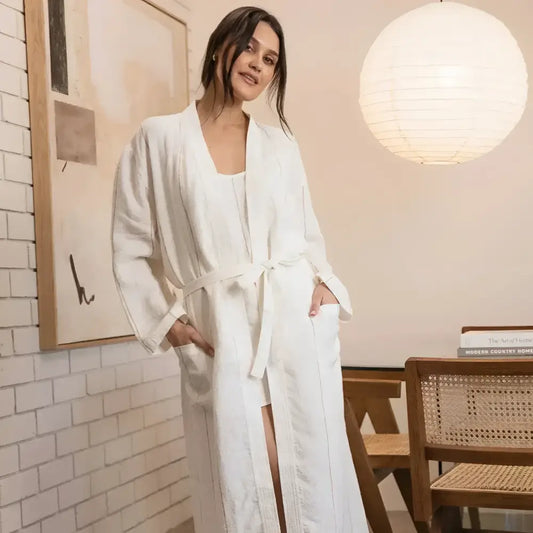 Woman wearing a white robe in a room with a lamp and chair.