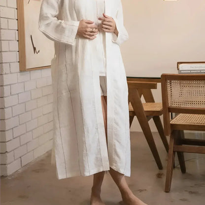 Person wearing a white robe in a room with wooden furniture and a white wall.