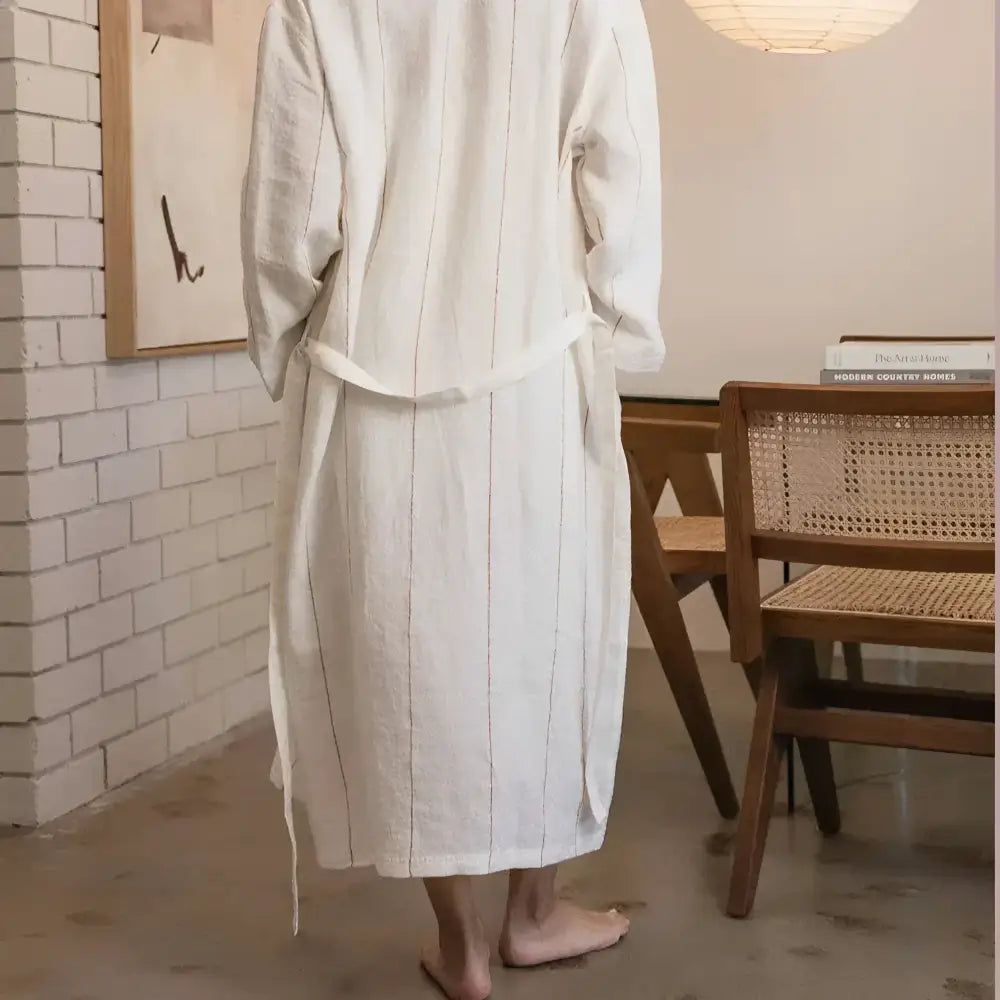 Person wearing a white striped robe in a room with wooden furniture and a tiled wall.