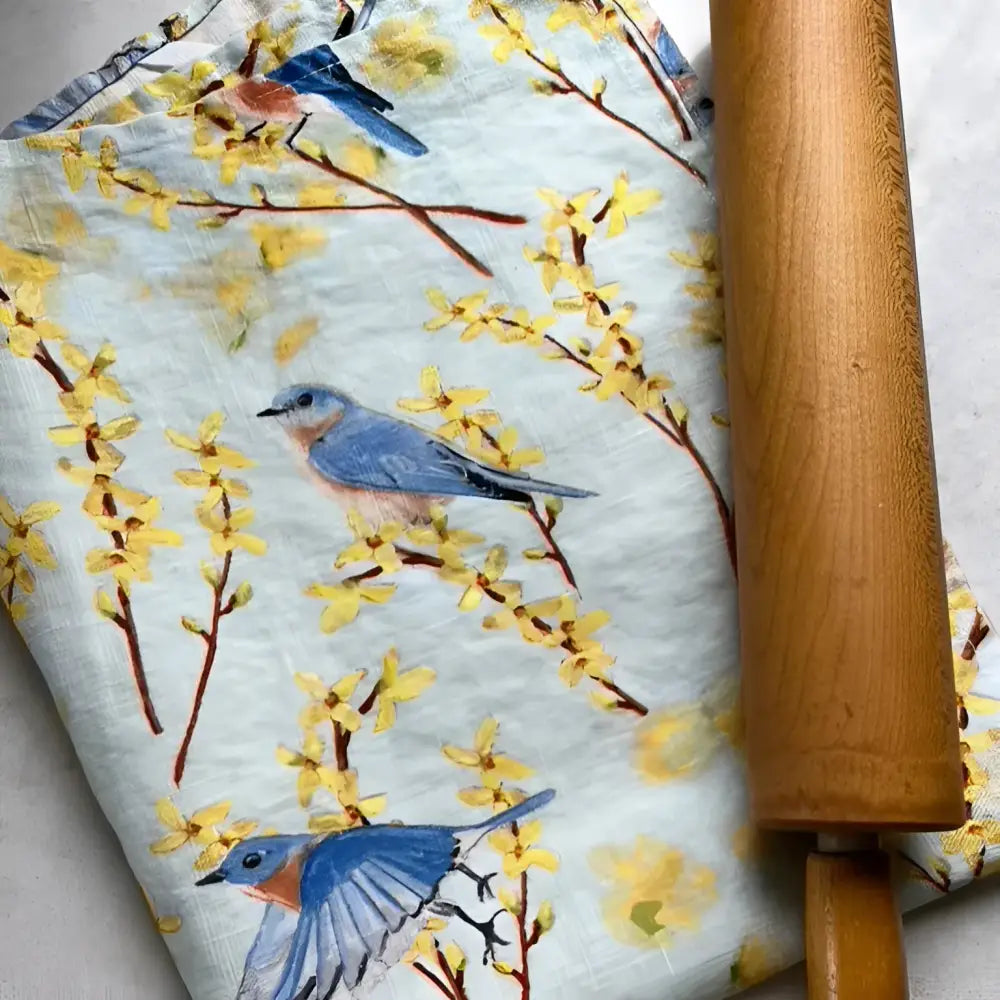 Floral and bird-patterned fabric with a wooden rolling pin on a light background