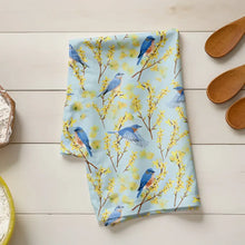 Floral towel with blue birds on a wooden surface with flour and wooden spoons.