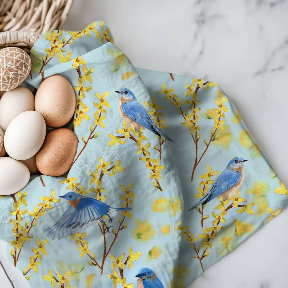 Basket of eggs on a floral towel with blue birds on a marble surface