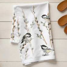 Kitchen towel with bird design on a wooden surface with flour and wooden spoons.