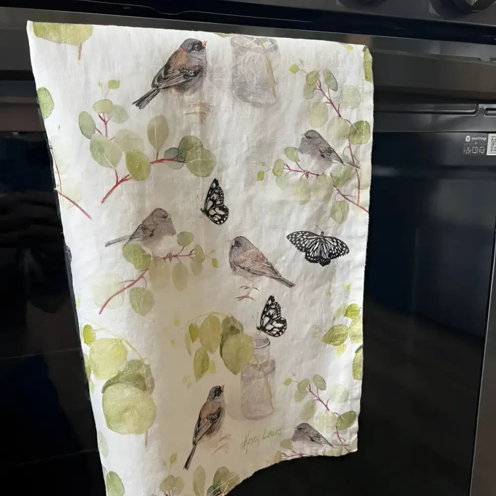 Decorative kitchen towel with nature-themed design hanging on a stove handle.