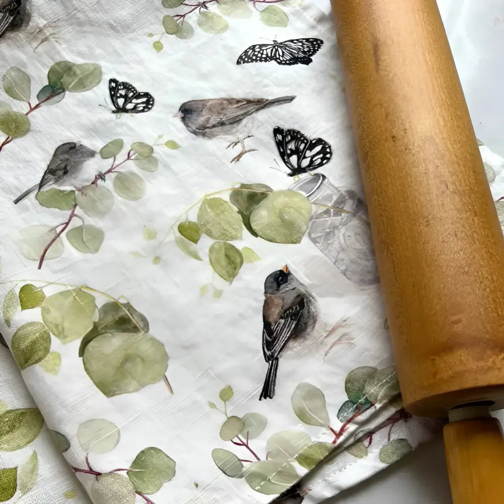Wooden rolling pin next to a nature-themed design featuring birds and leaves