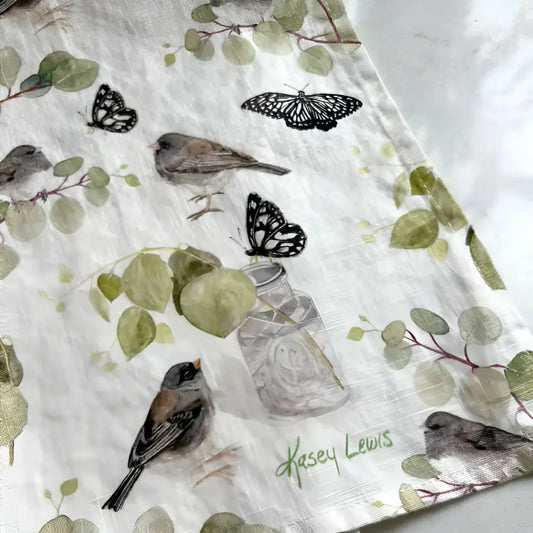 Fabric with nature-themed design featuring birds, butterflies, and plants on a white background.