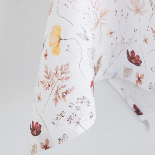 100% linen tea towel with a white base color and has flowers and leaves printed in varying colors throughout.