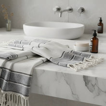 A white and gray linen turkish bath towel with black geometric stripes and fringed tassel edges perfect for bath use