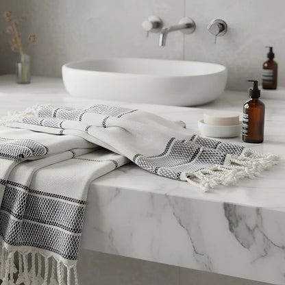A white and gray linen turkish bath towel with black geometric stripes and fringed tassel edges perfect for bath use