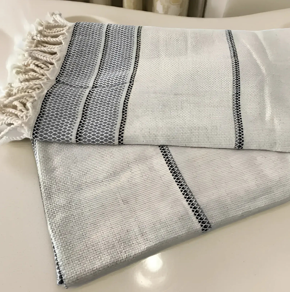 A soft off-white linen turkish bath towel with textured weave gray stripes and black mesh detailing on edges
