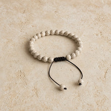 A delicate white lotus seed mala bracelet with speckled beads and a black macrame knot with adjustable cord ends