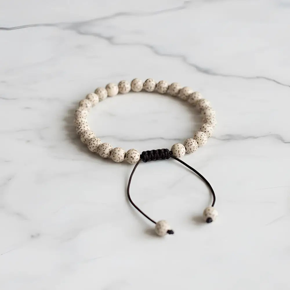 Beige speckled lotus seed mala bracelet with black macrame knot and adjustable cord for easy wear
