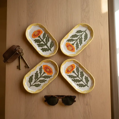 Four oval handcrafted ceramic trinket dishes with orange poppy flowers and yellow textured rims on speckled white background