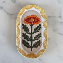An oval handcrafted ceramic trinket dish with a marigold flower and golden-yellow border perfect for small items