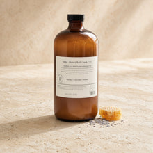 A 40oz bath soak in an amber glass bottle with a black cap labeled milk and honey bath soak by baude laire