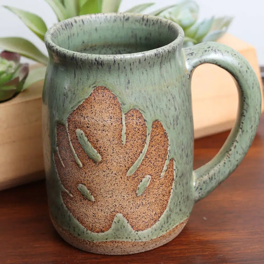 Speckled stoneware green mug with brown monstera leaf design.