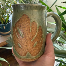 Speckled stoneware green mug with brown monstera leaf design.