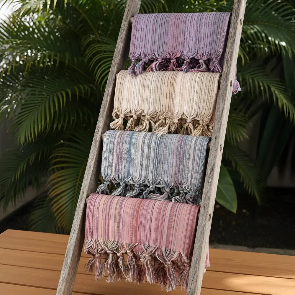 A set of colorful turkish beach towels with soft pastel stripes tassels and fringed edges displayed on a wooden ladder